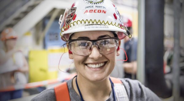 A close-up of Jamie wearing safety glasses and a hard hat