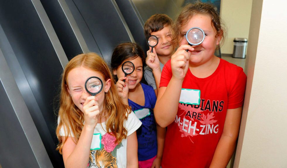 A group of children peer through magnifying glasses at a community activity.