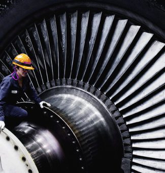 A female worker wearing protective clothing on top of a huge turbine in a nuclear power station.