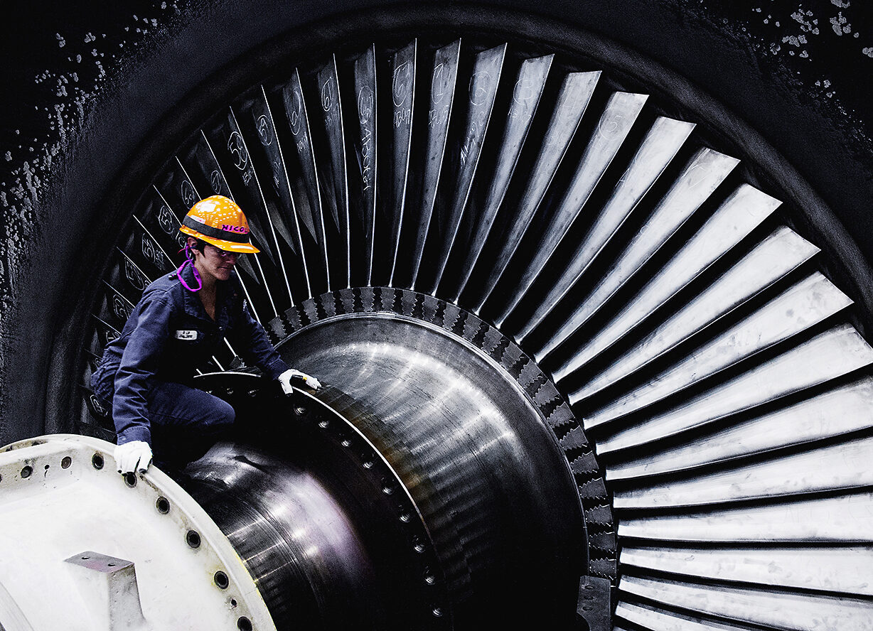 A female worker wearing protective clothing on top of a huge turbine in a nuclear power station.