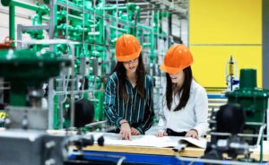 Two female workers in hard hats examine plans on a table.