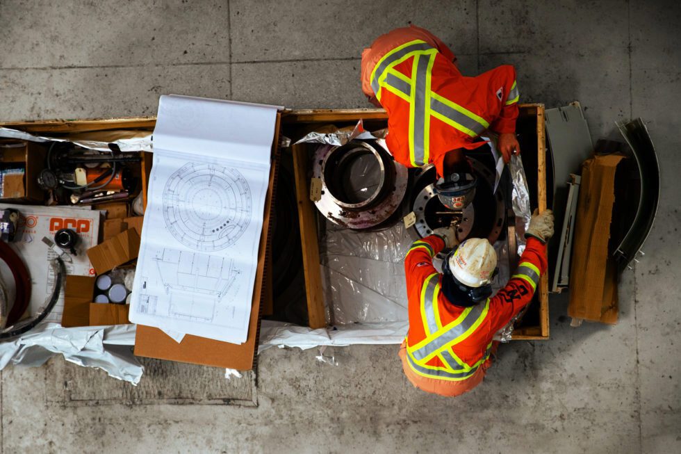 Workers in safety vests and hard hats examine construction plans.