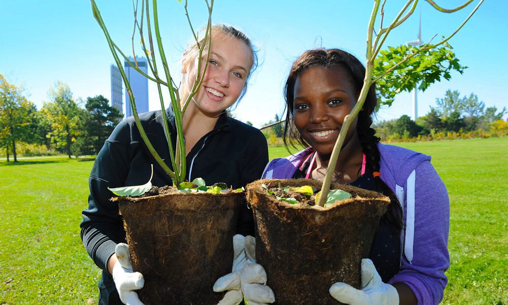 Two young girls hold tree saplings ready for planting.