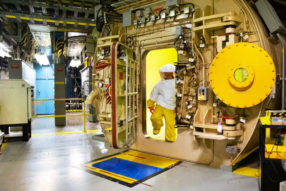 An worker in protective plastic clothing exits an airlock in a nuclear station.