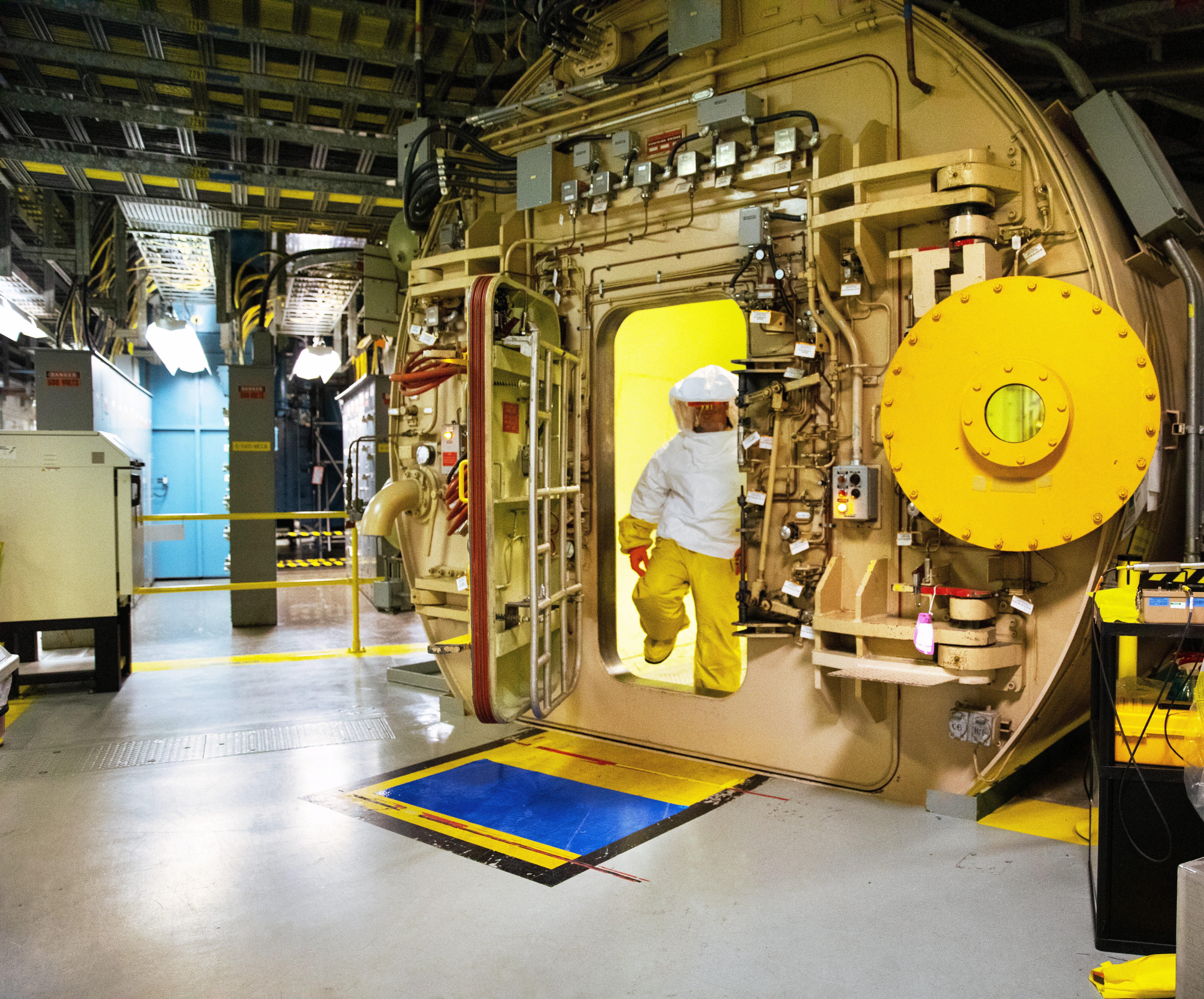 An worker in protective plastic clothing exits an airlock in a nuclear station.