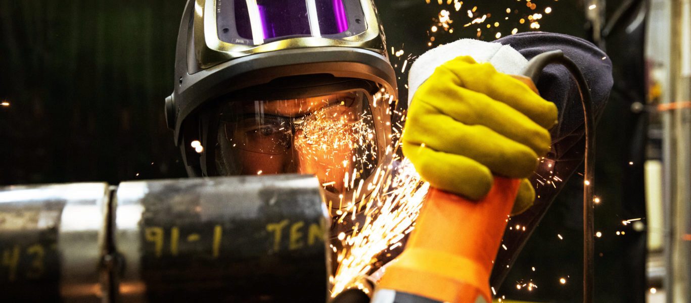 Sparks fly as a male worker in protective gear uses a grinder.