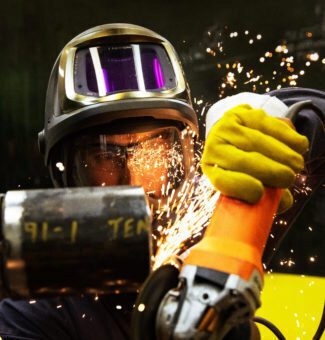 Sparks fly as a male worker in protective gear uses a grinder.