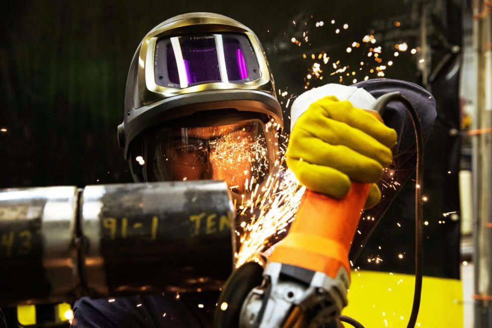 Sparks fly as a male worker in protective gear uses a grinder.