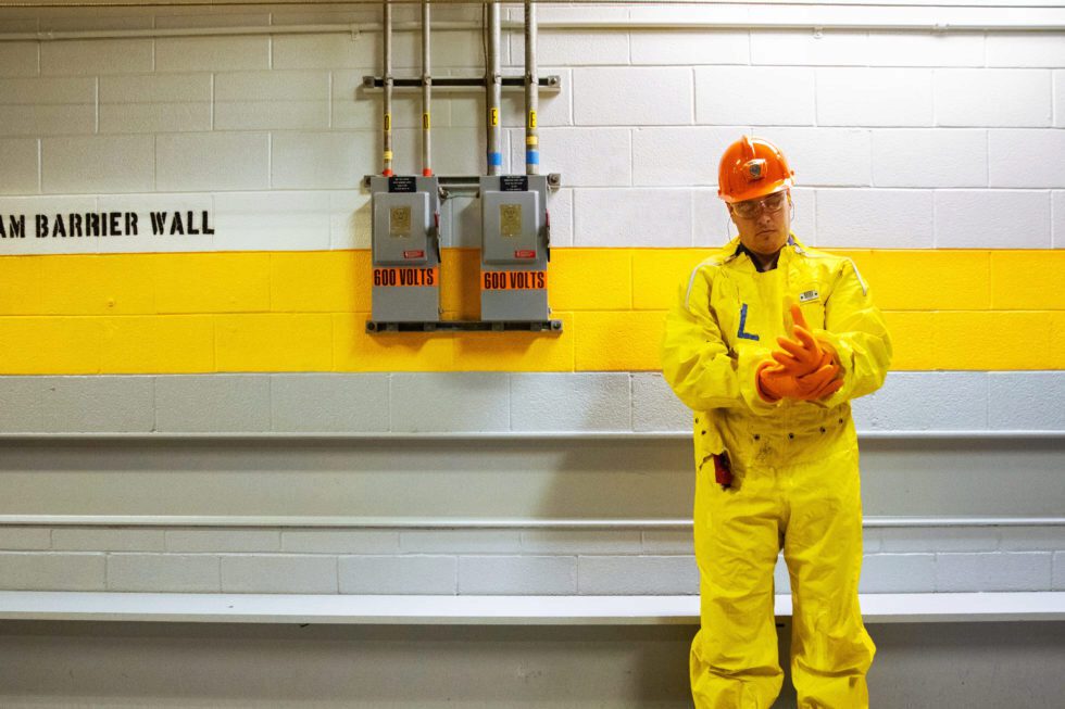 A male worker in protective plastic clothing stands in a hallway within the protected area of a nuclear station.