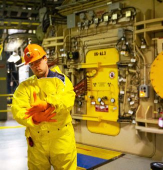 A worker in protective plastic clothing stands outside an airlock at the Pickering Nuclear Generating Station.