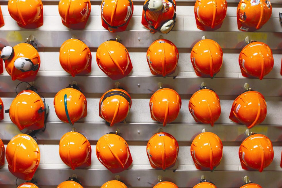 A large collection of orange hard hats hanging on a wall.