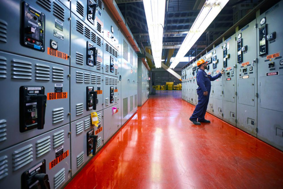 A male worker in coveralls and hard hat on a turbine floor at a power station.