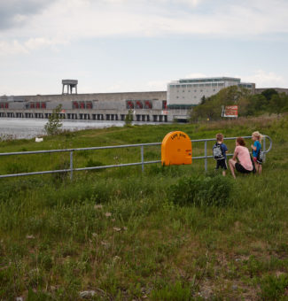 A young family stands at a fence looking at the RH Saunders Generating Station.