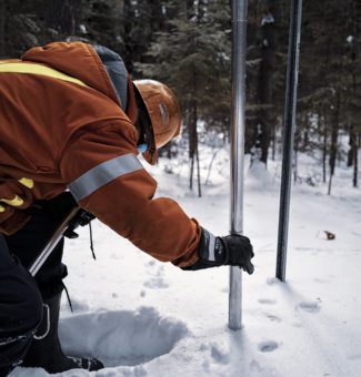 An employee performs a snow survey measurement.