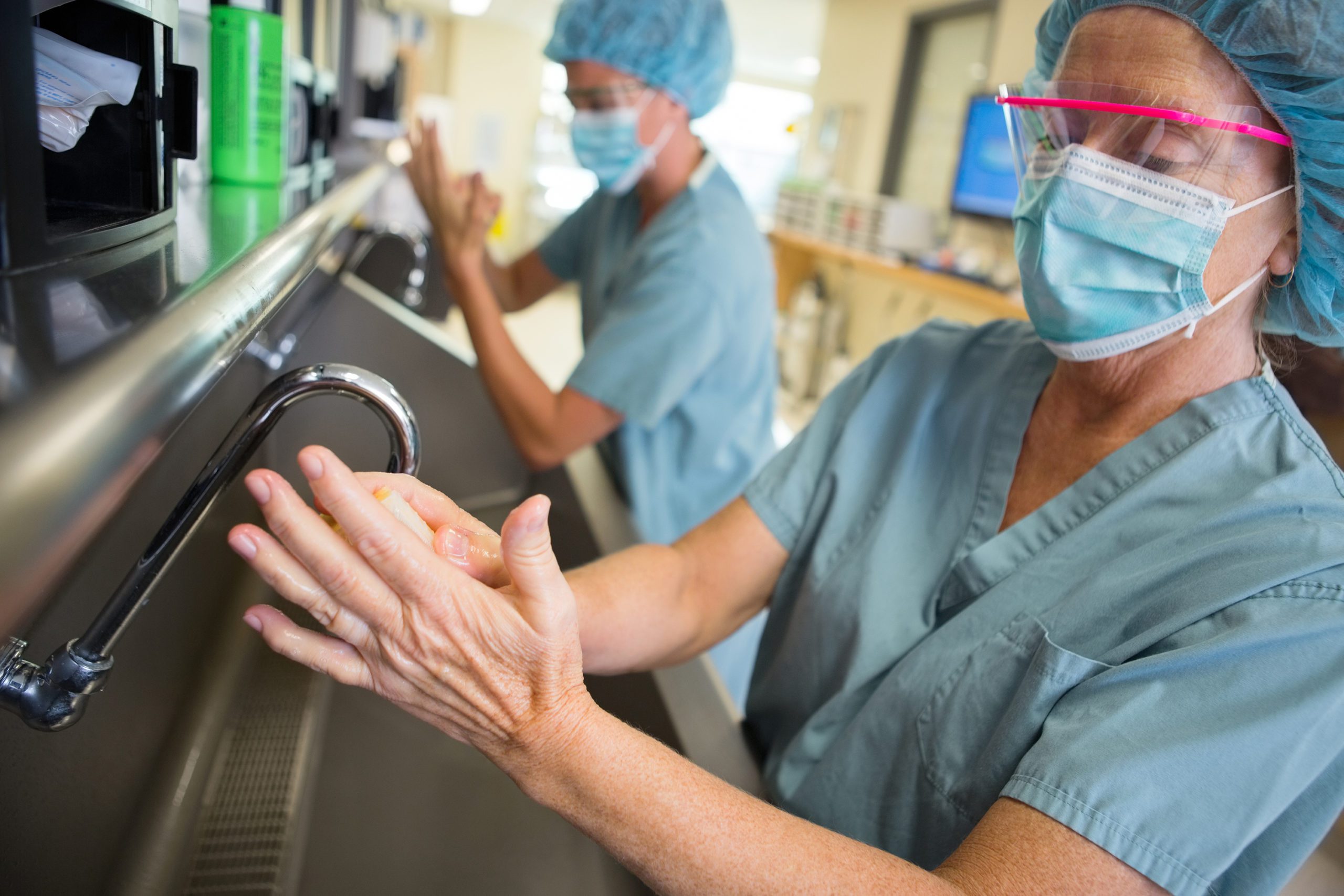 Healthcare workers wearing surgical masks scrubbing their hands.