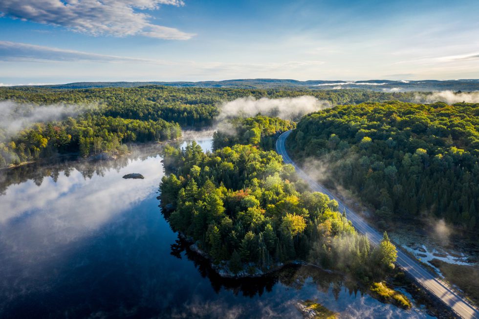 Aerial view of a country highway by a lake and through a forest on a misty morning