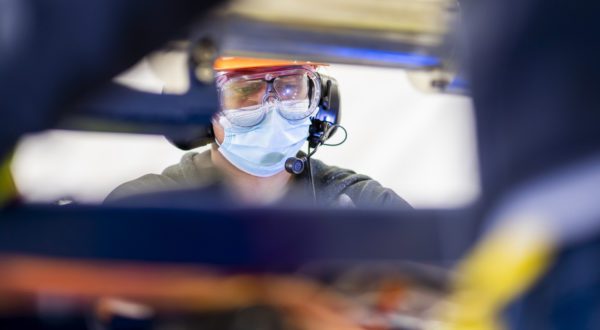 A worker in a mask and safety goggles wearing a telecommunications headset.
