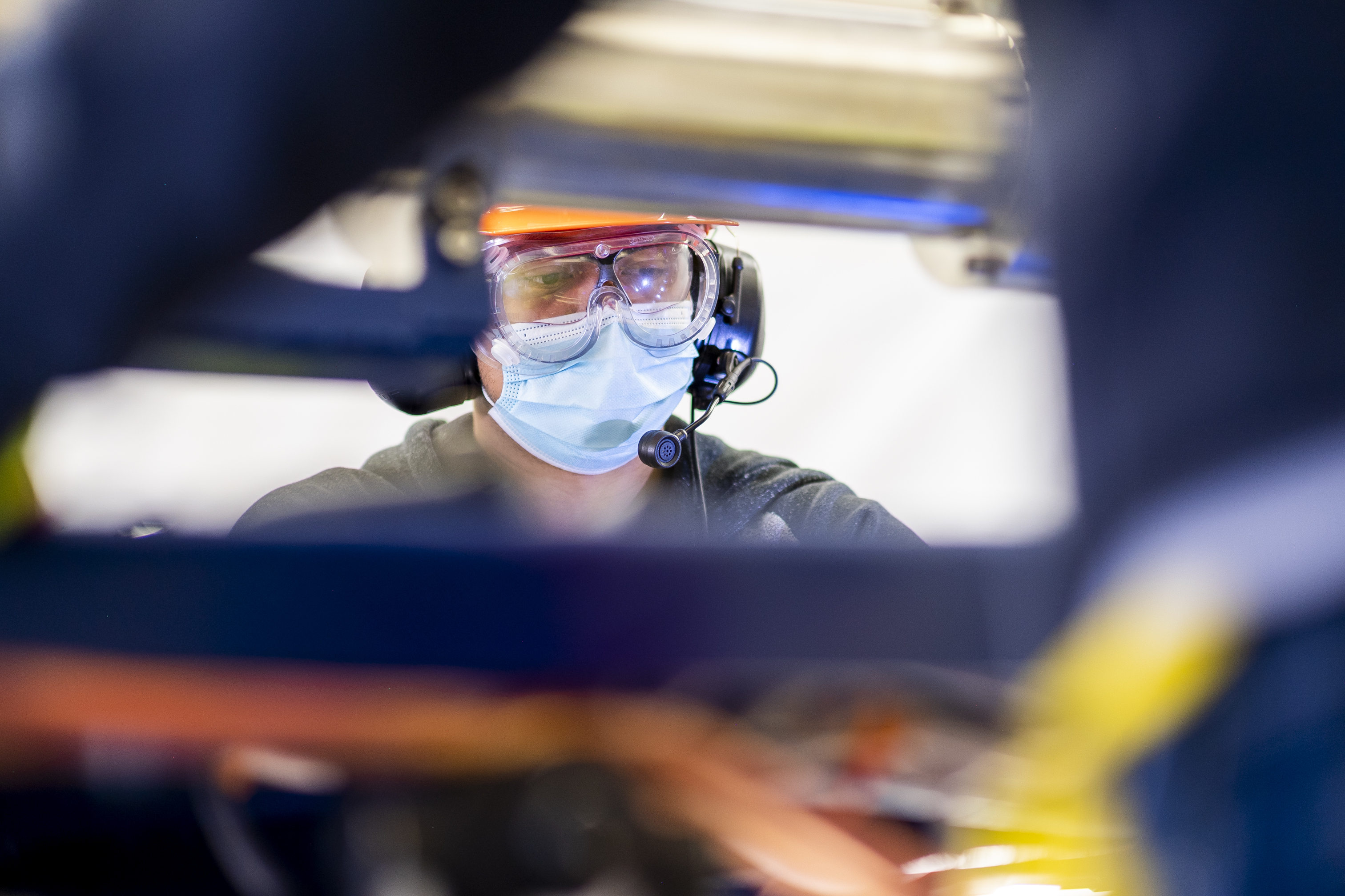 A worker in a mask and safety goggles wearing a telecommunications headset.