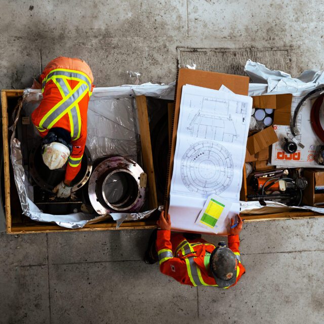 Workers in safety vests and hard hats examine construction plans.