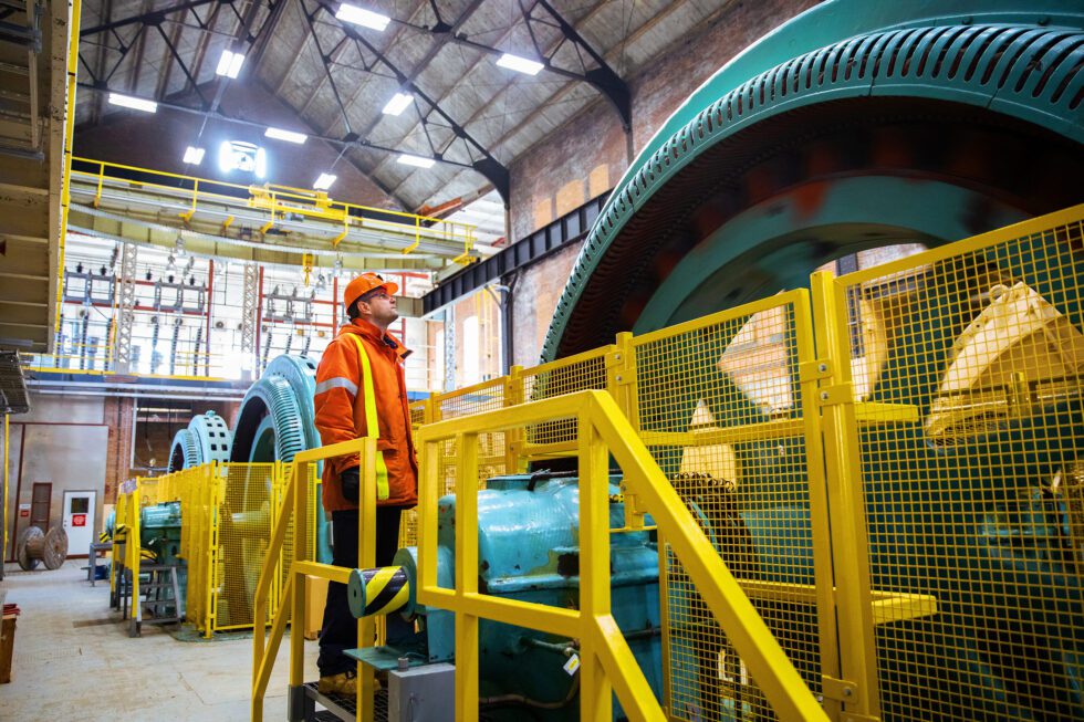 A worker in orange protective gear examines a turbine at Ranney Falls hydroelectric station.