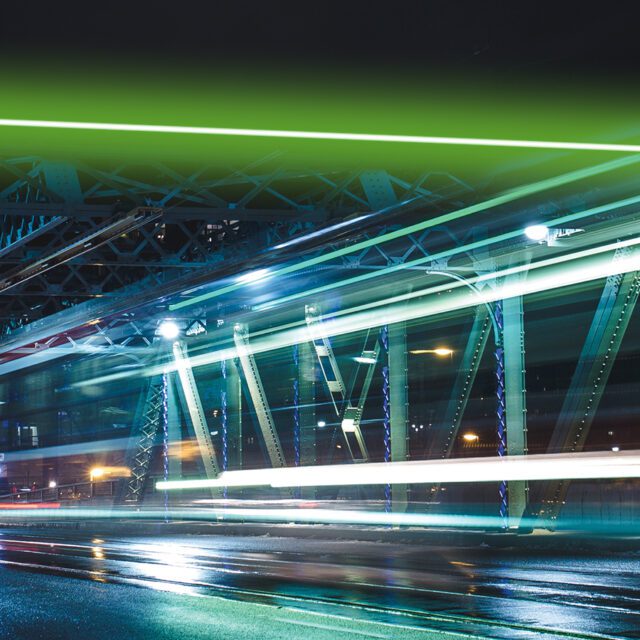 An electric streercar blurs over a city bridge at night.