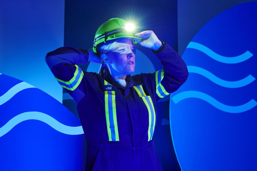 A female employee in protective gear adjusts her hard hat.