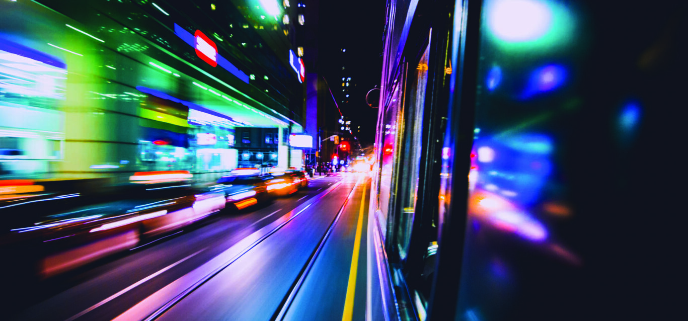 Fast-motion public transit vehicle speeding down street core with beautiful color streaks. Train transportation.