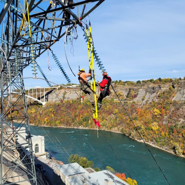 Workers are seen using a suspended ladder and safety harnesses as they replace insulators that have reached the end of their service life at Sir Adam Beck II Generating Station in Niagara Falls.