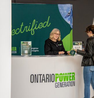 A member of the public stands at an OPG-branded information booth discussing a topic of interest.