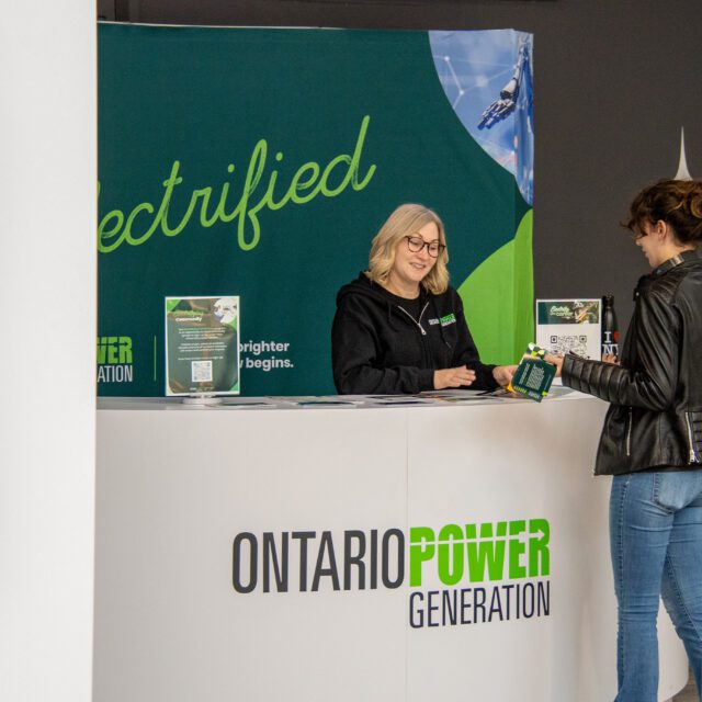 A member of the public stands at an OPG-branded information booth discussing a topic of interest.