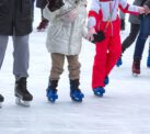 Feet of different people skating on the ice rink