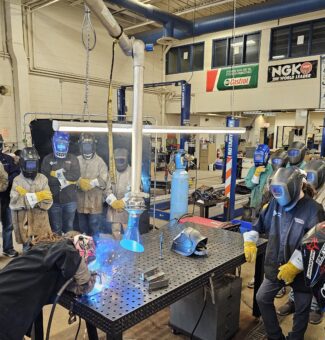 Students in protective gear watch a welding demonstration at the Mind Over Metal camp.