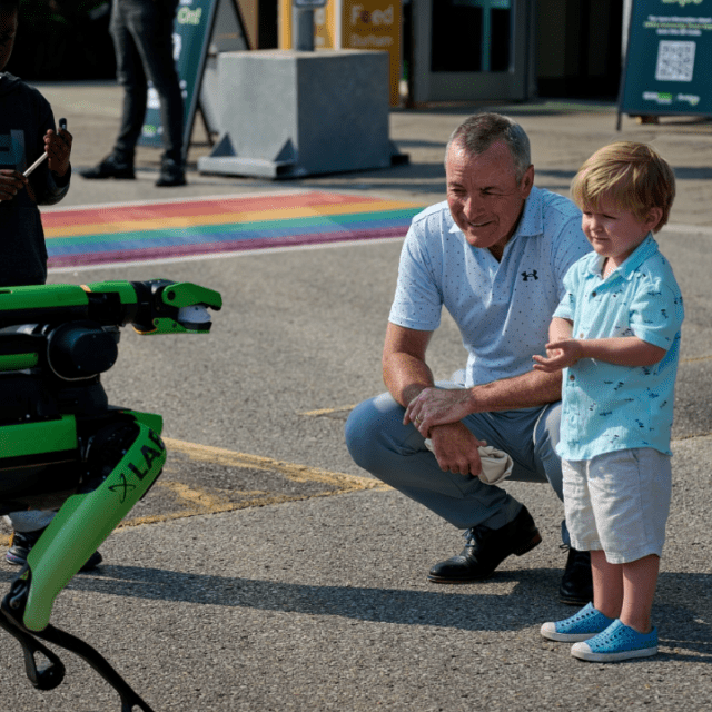 President & CEO, Ken Hartwick, and a child examine Spot; a robotic dog.