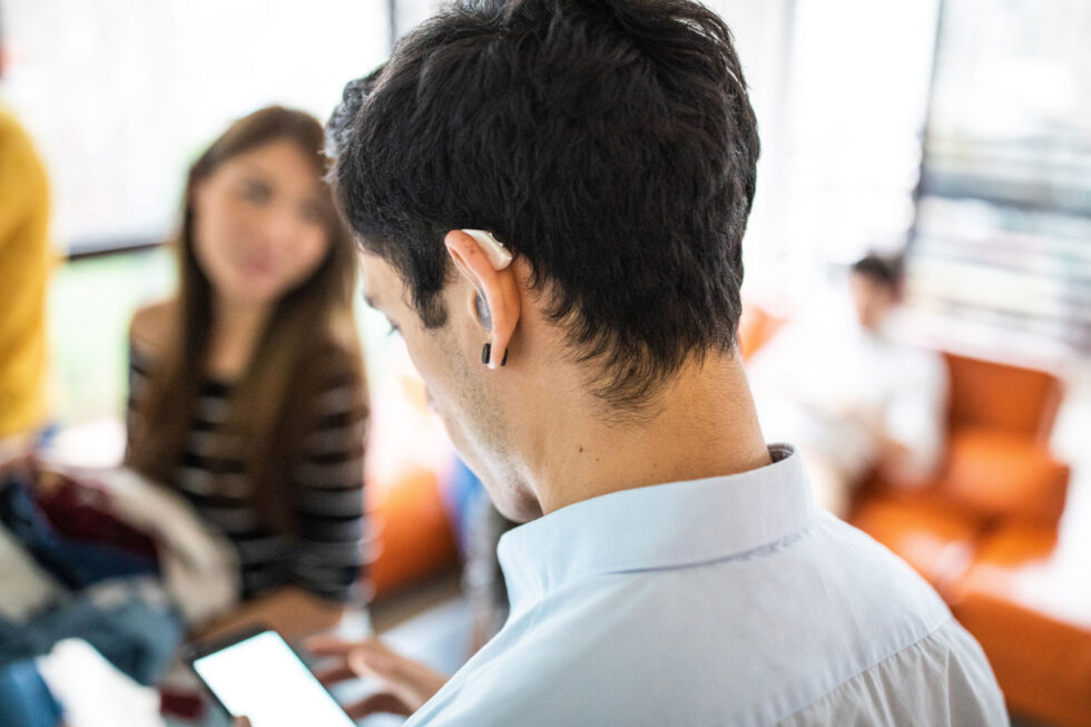 A man wearing hearing assistance speaks to colleagues.